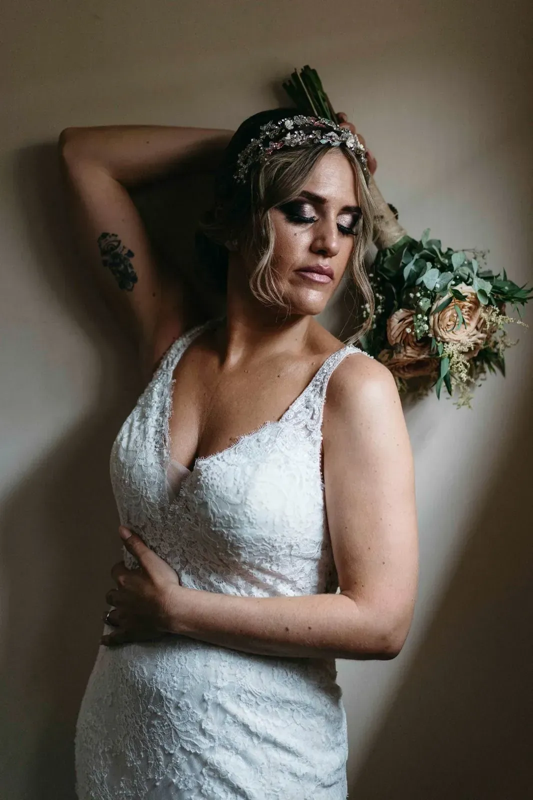 Novia con un vestido blanco de encaje, posando en interiores con un ramo de flores y un tocado enjoyado