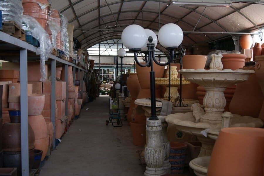 Pasillo de mercado de cerámica protegido, bordeado de macetas de terracota y jardineras con pedestal bajo un techo curvo