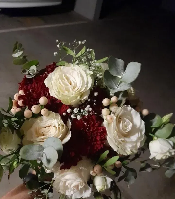 Ramo floral blanco y burdeos con eucalipto y toques de frutos rojos sobre un fondo oscuro