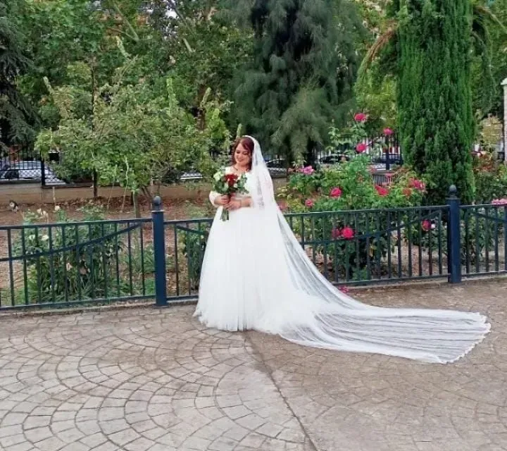 Novia con vestido blanco y velo largo sosteniendo un ramo en un parque con jardín