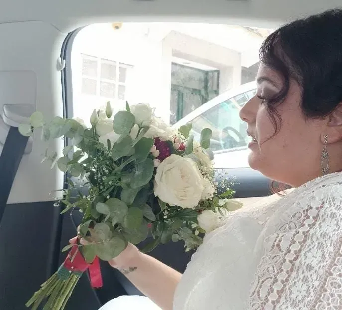 Una novia sostiene un ramo blanco dentro de un coche, vista de perfil desde el asiento trasero