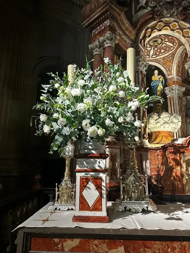 Arreglo floral blanco sobre un altar con una ornamentada decoración religiosa dorada en una iglesia