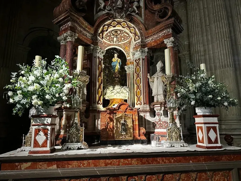 Altar de iglesia ornamentado con una estatua religiosa, velas y grandes arreglos florales blancos