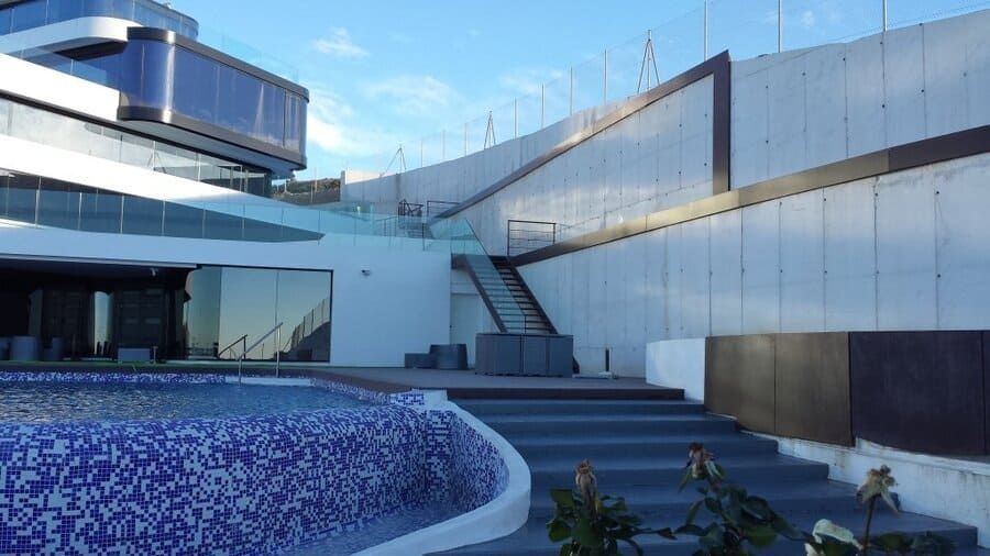 Edificio blanco moderno con una piscina azul curvada y una escalera exterior bajo un cielo despejado