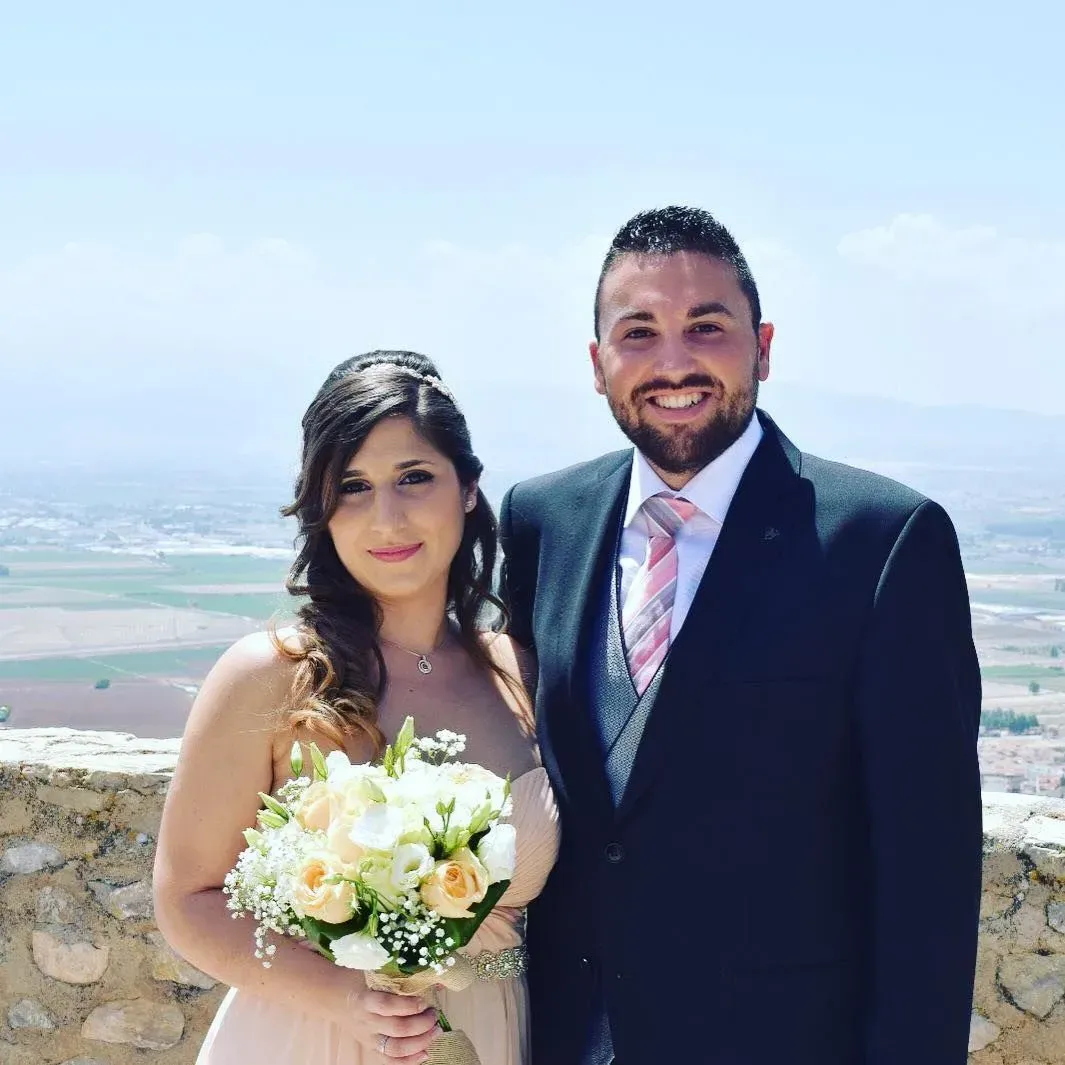 Pareja vestida de etiqueta posando al aire libre con un ramo y un paisaje de fondo