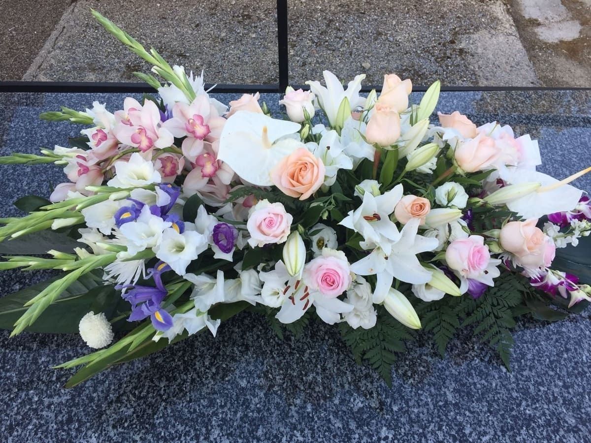 Arreglo floral con lirios blancos, rosas rosas y toques morados sobre un pavimento de piedra
