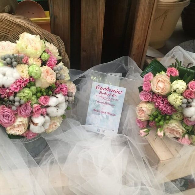 Tres ramos de flores en tonos pastel envueltos en tul blanco, colocados sobre cajas de madera con un pequeño cartel en el centro, entre ellos