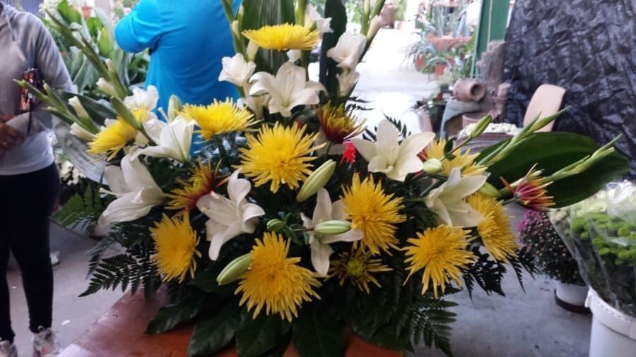 Arreglo floral amarillo y blanco con follaje verde en un puesto de un mercado al aire libre