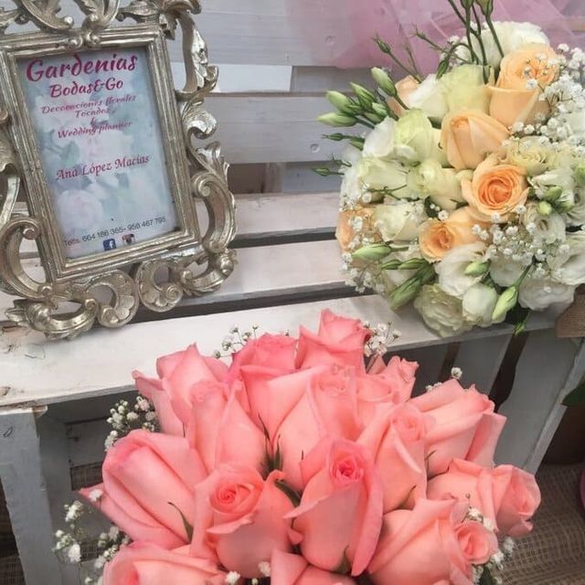 Ramos de rosas rosas y color crema junto a un cartel con un marco ornamentado sobre un banco blanco