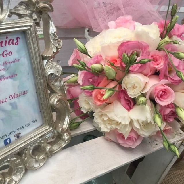 Ramo de rosas rosas y blancas junto a un marco plateado ornamentado sobre una mesa
