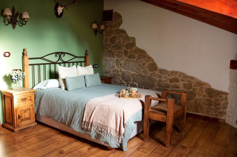 Dormitorio con pared de piedra, cama de madera, pared verde, ropa de cama azul y una pequeña silla de madera.