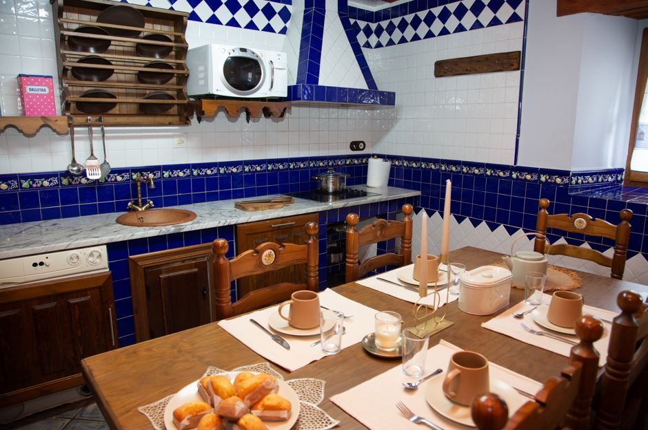 Cocina rústica con paredes de azulejos azules, mesa de madera preparada para comer, microondas y estufa empotrada.