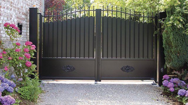 Superbe portail battant en acier noir et jolies fleurs à l'entrée du jardin