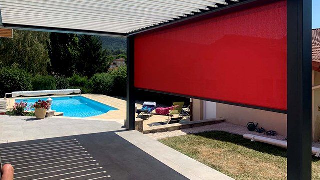 Focus sur une pergola bioclimatique design noire et pan de mur rouge