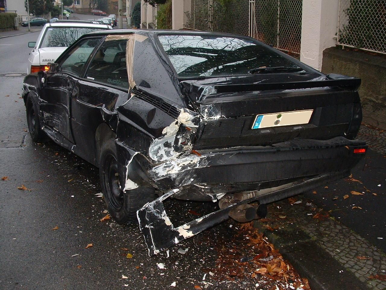 Am Straßenrand steht ein schwarzes Auto, das bei einem Unfall beschädigt wurde