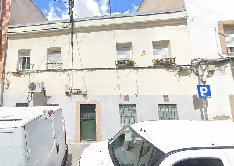 Una camioneta blanca está estacionada frente a un edificio al lado de una señal de estacionamiento.