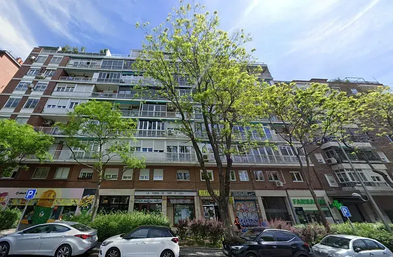 Un edificio con muchas ventanas y coches aparcados delante de él.