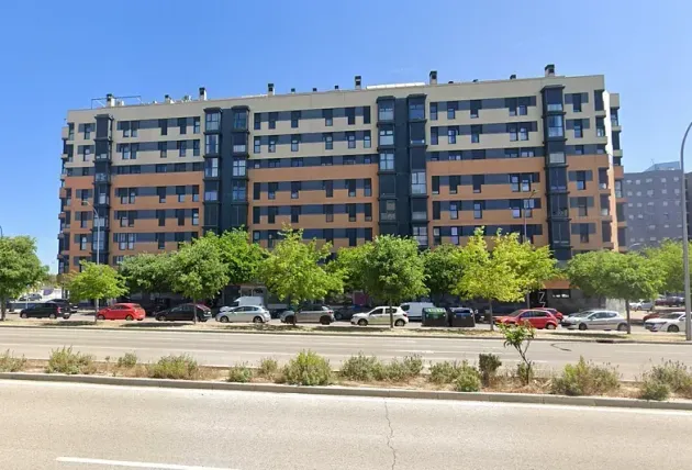 Un gran edificio de apartamentos con coches aparcados delante.