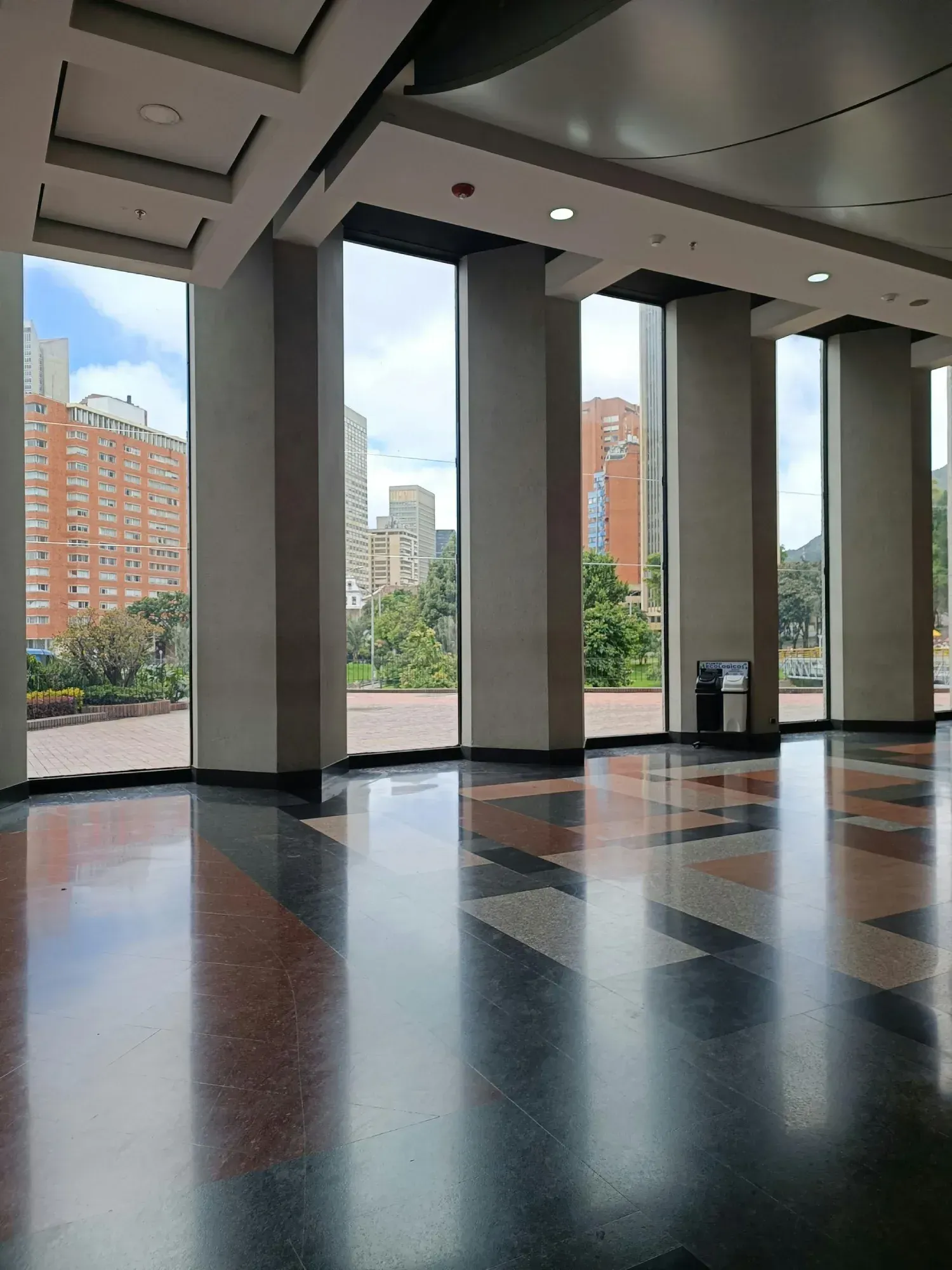 Vista, a través de grandes ventanales que van del suelo al techo, de una ciudad con edificios altos.