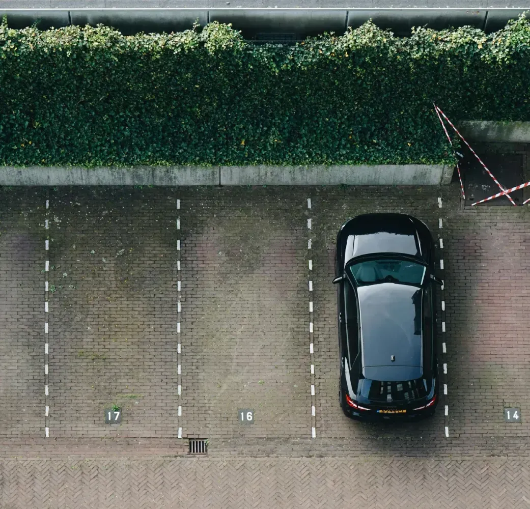 Un coche negro aparcado en un aparcamiento pavimentado con plazas numeradas, visto desde arriba.