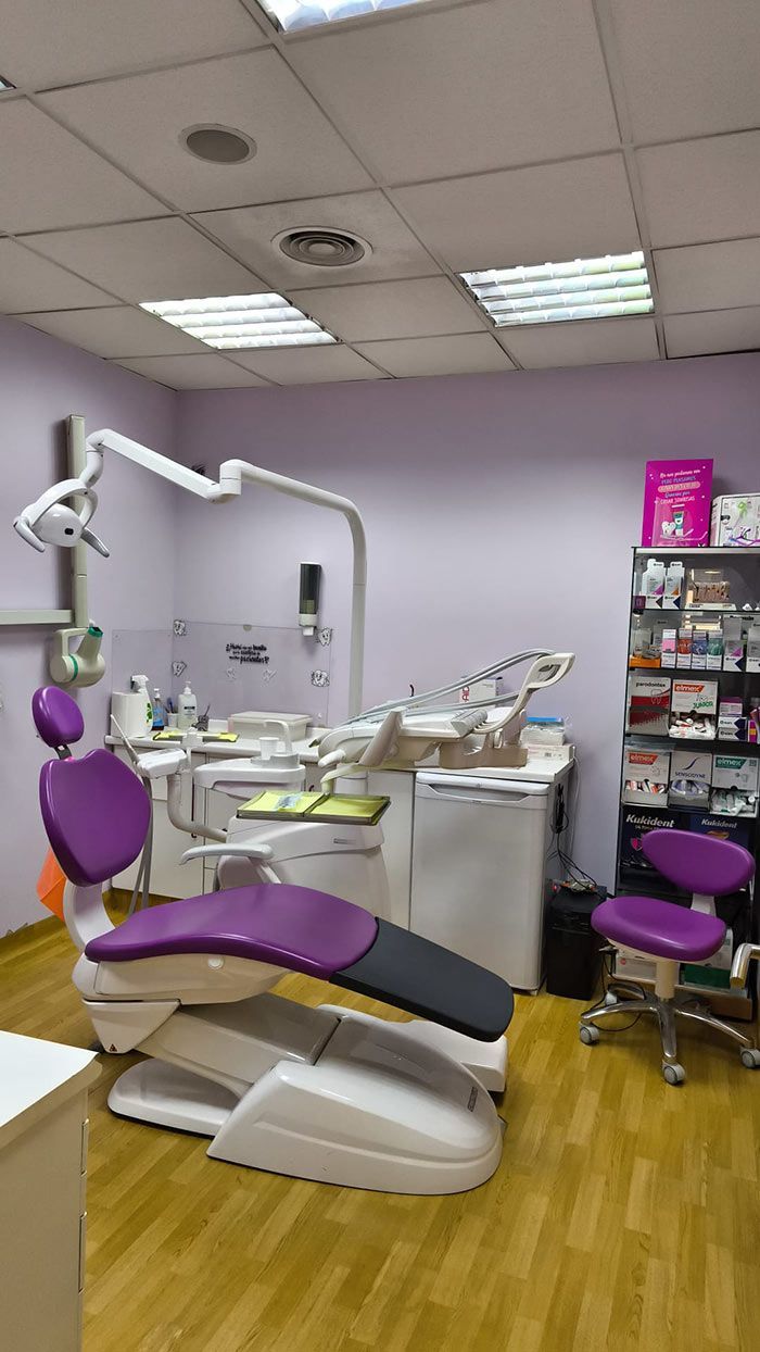 Sala de examen dental con sillón morado para el paciente, instrumental dental y armarios bajo luces fluorescentes brillantes.