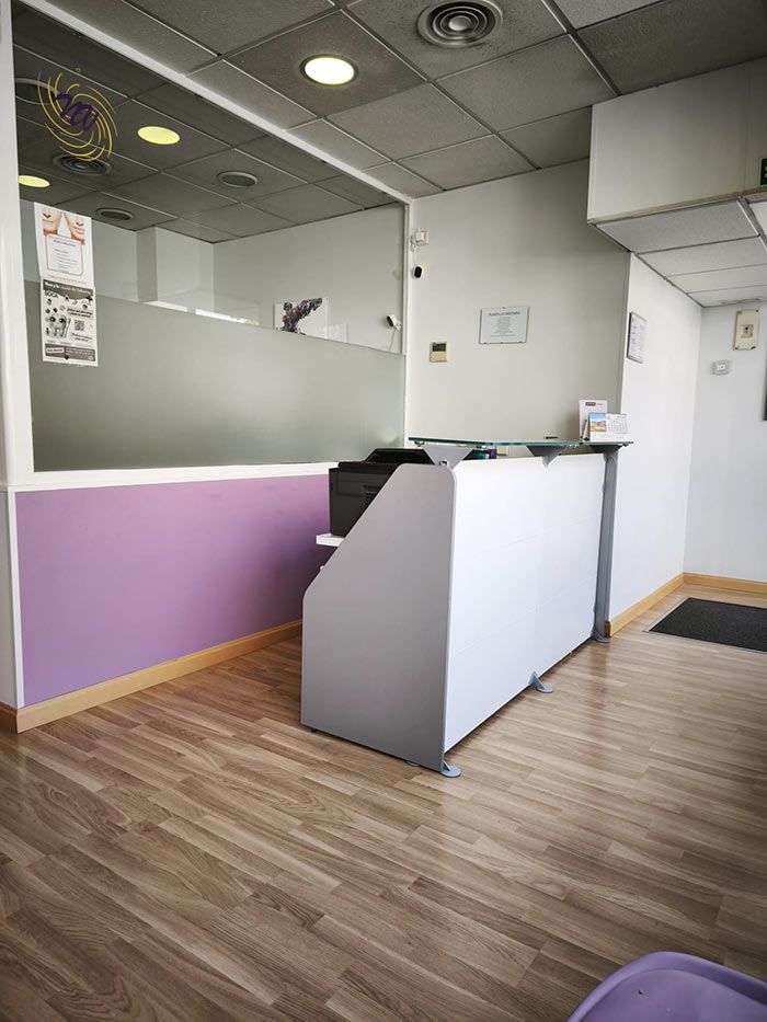 Área de recepción de oficina vacía con una pared decorativa de color púrpura, mostrador blanco y suelo que imita la madera.