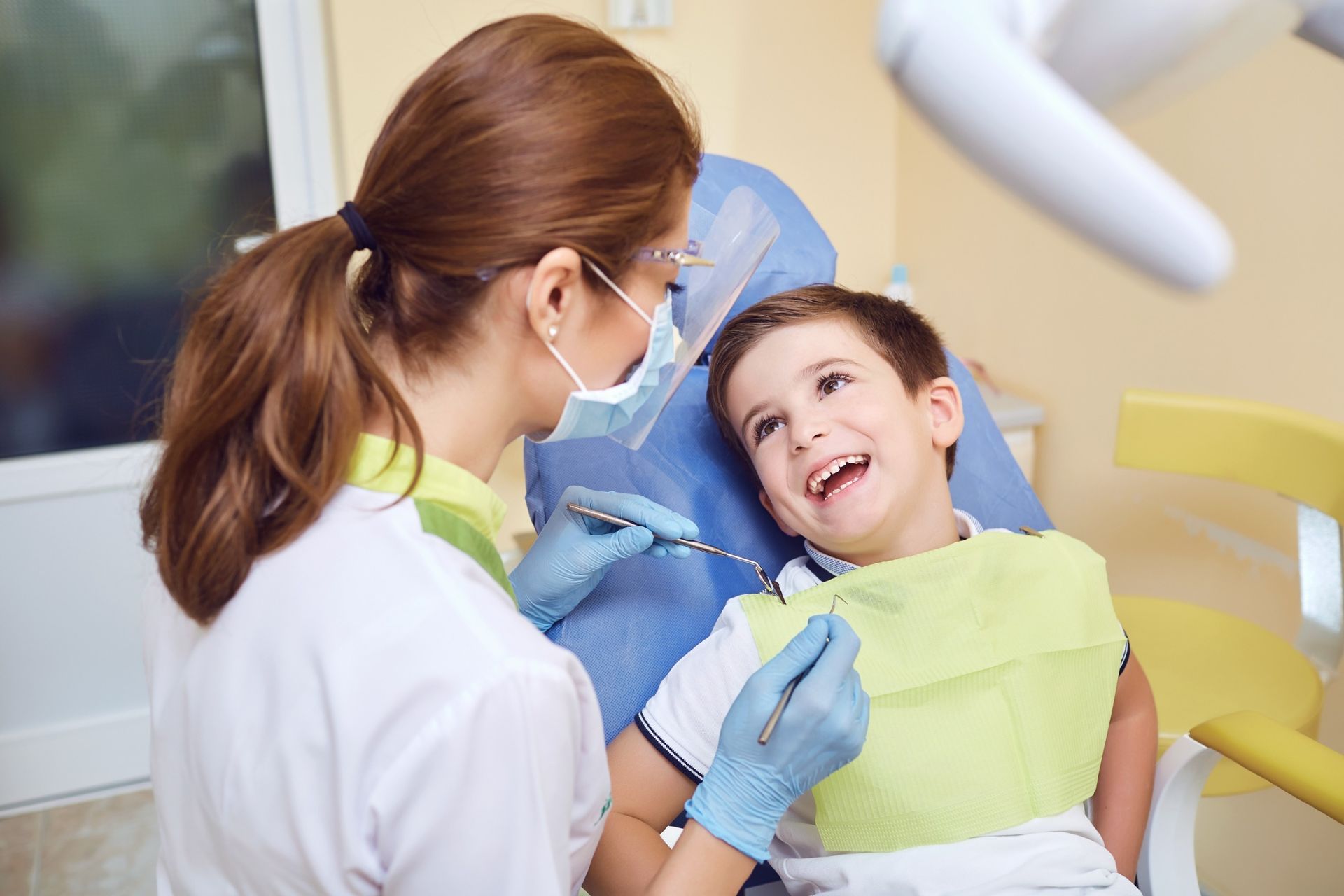 Un dentista examina a un niño sonriente en el sillón dental, con mascarilla y guantes azules.