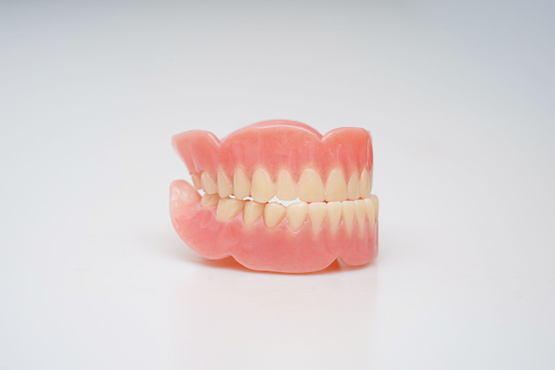 Prótesis dentales rosas y blancas sobre un fondo blanco liso.