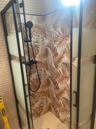 Una cabina de ducha con un marco negro y un papel tapiz con hojas en la pared.