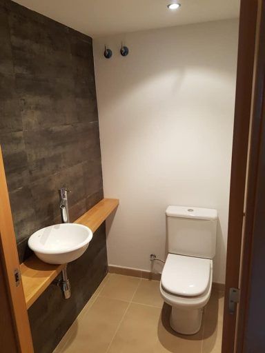 Un baño con inodoro, lavabo y estante de madera.