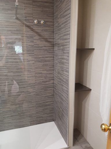 Un baño con ducha a ras de suelo y estanterías.