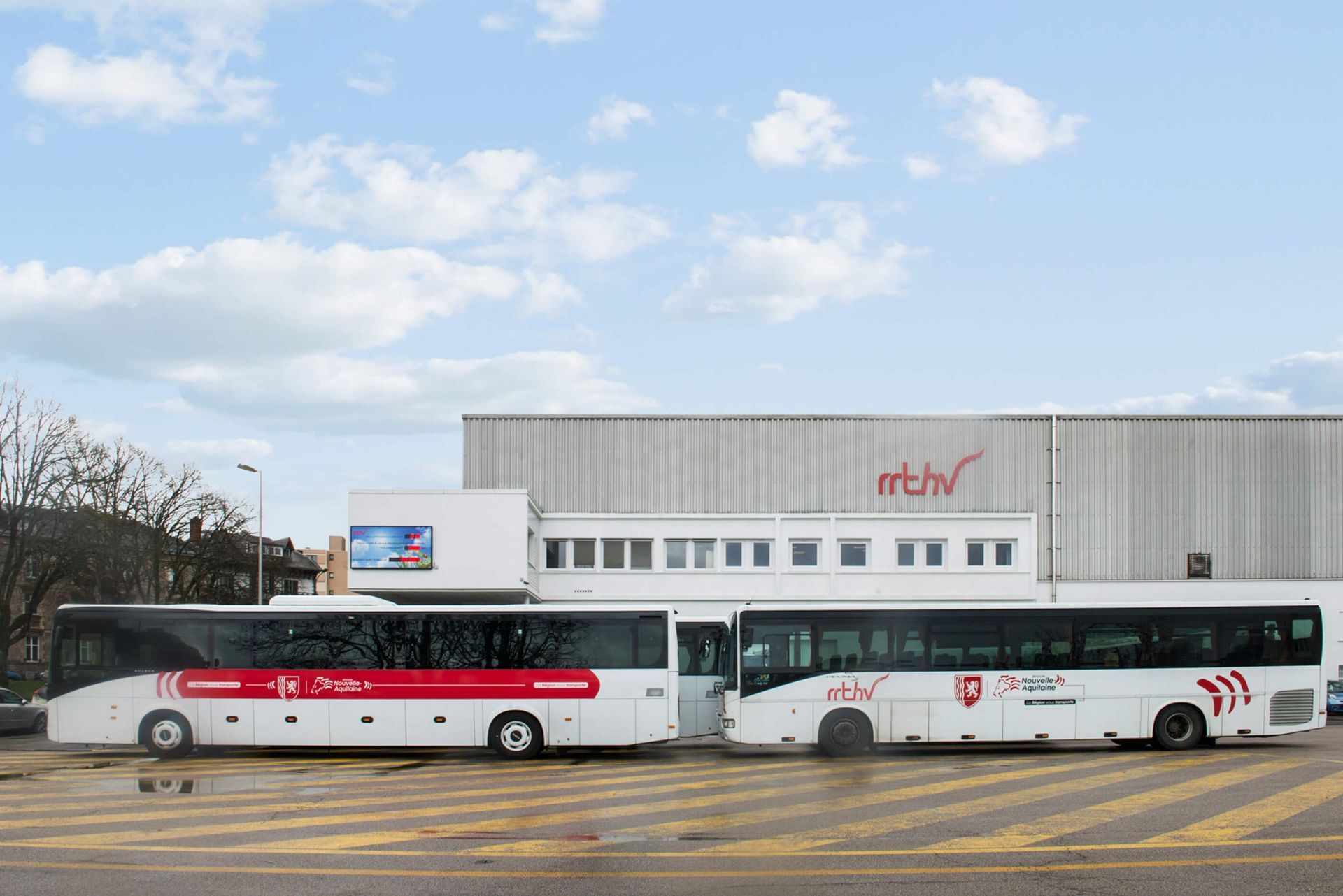 Deux bus blancs sont stationnés devant un bâtiment blanc portant l'inscription « mtv ». L'un des bus a une bande rouge.