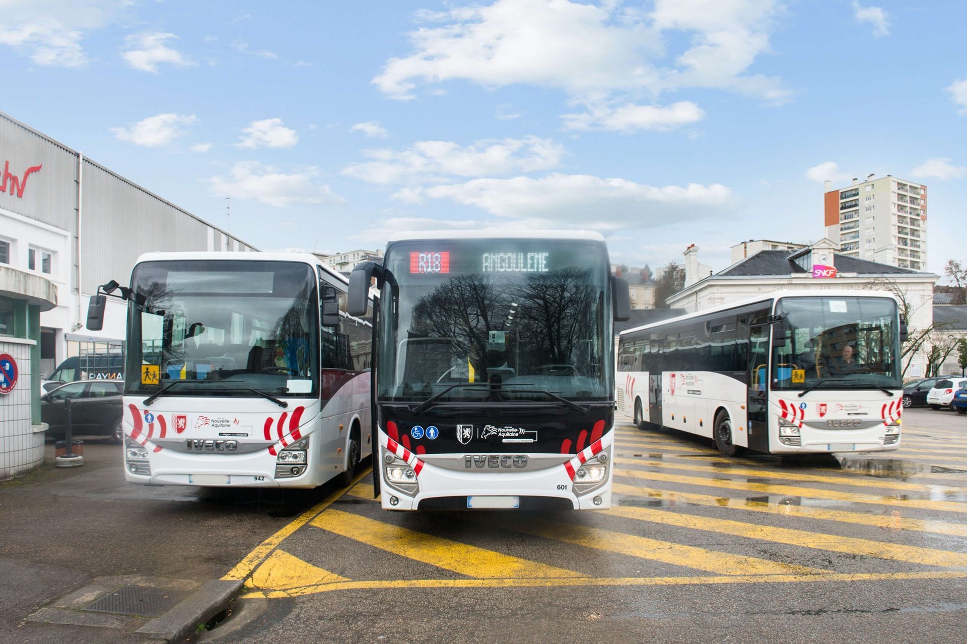 Trois autobus blancs stationnés dans un dépôt par temps nuageux.