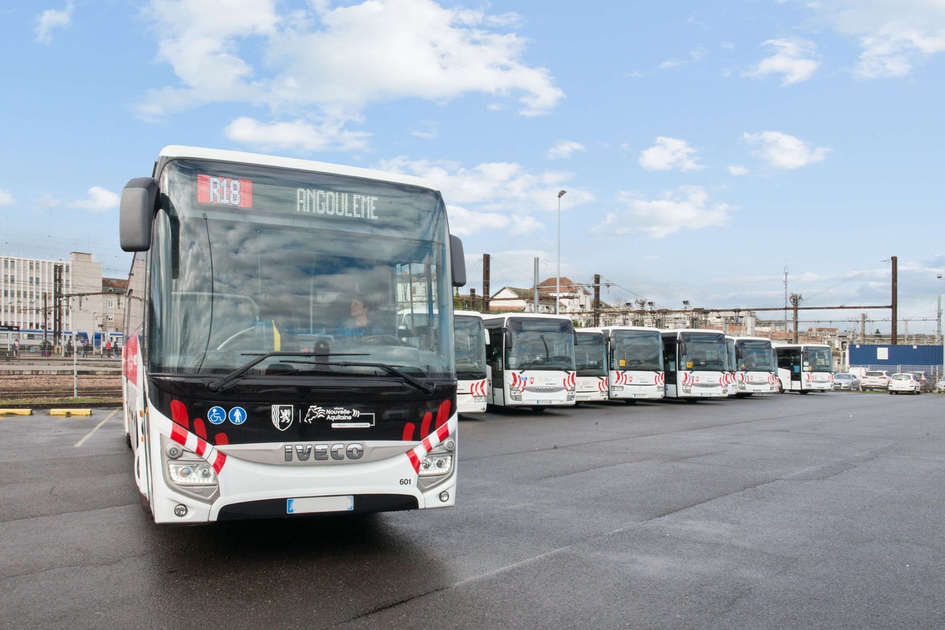 Une rangée de bus blancs stationnés sur l'asphalte. Le premier bus affiche « 606 » et « ROCHEFORT » à l'avant.