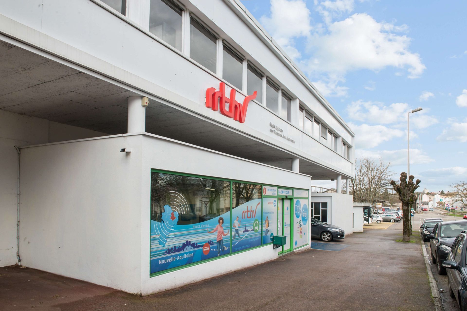 Bâtiment blanc avec logo rouge « ntkr », fresque murale, fenêtres, voitures garées.