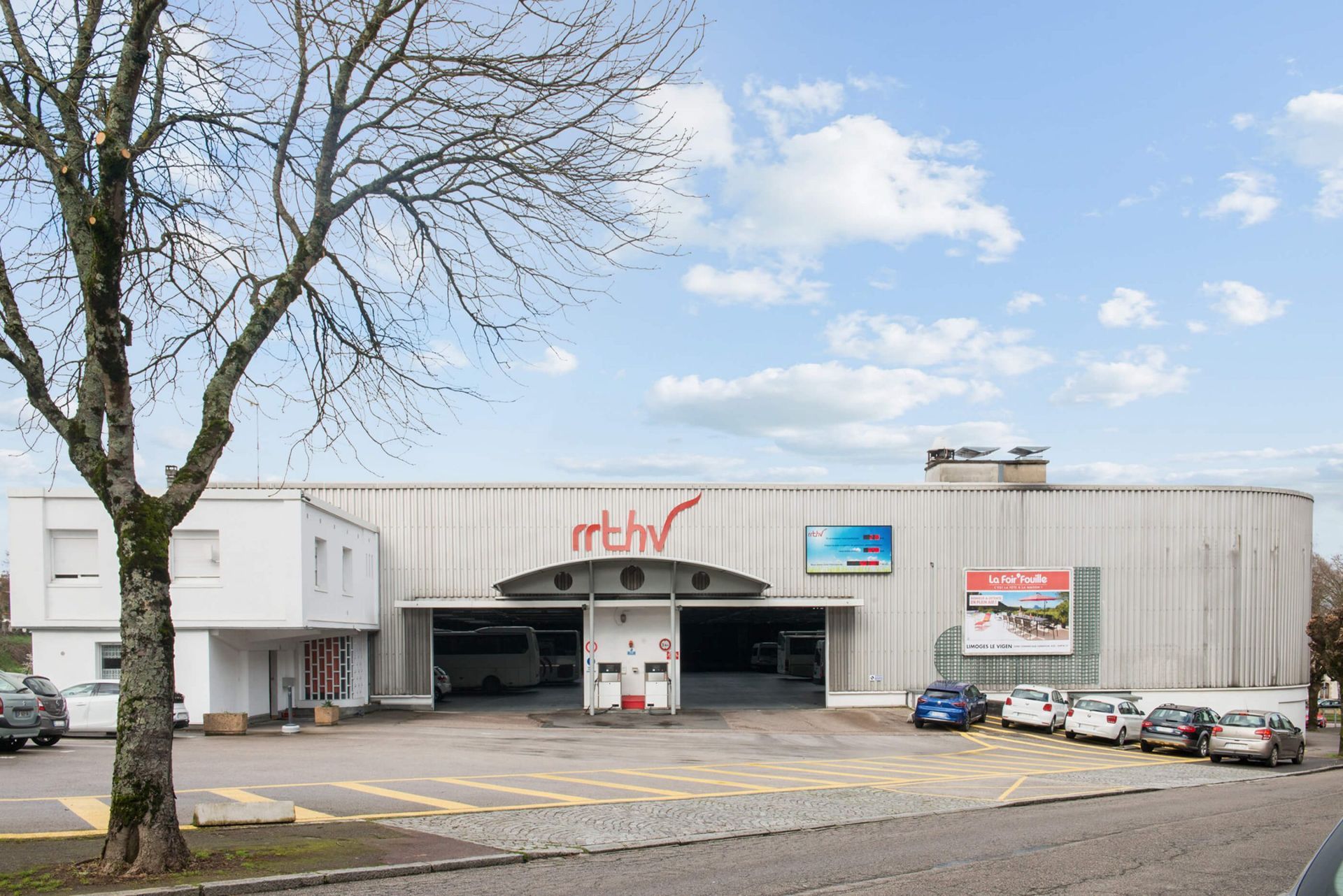 Extérieur du centre de services automobiles RTS, avec des véhicules stationnés, un ciel partiellement nuageux et le logo du bâtiment.