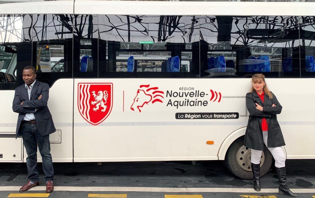 Deux personnes se tiennent près d'un bus, devant un immeuble. Le bus porte le logo de la Nouvelle-Aquitaine.