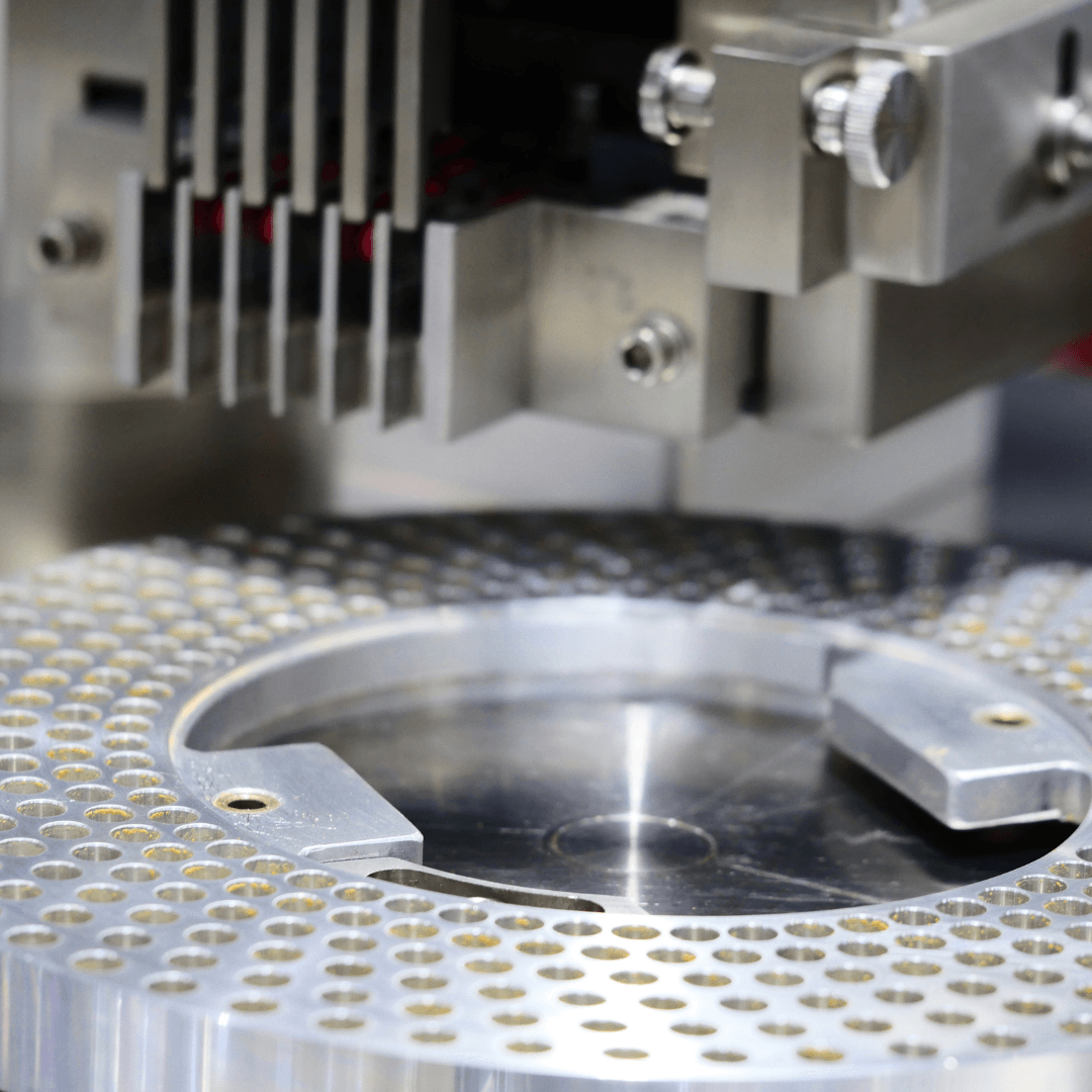 Primer plano de una máquina farmacéutica llenando cápsulas en una placa metálica giratoria.