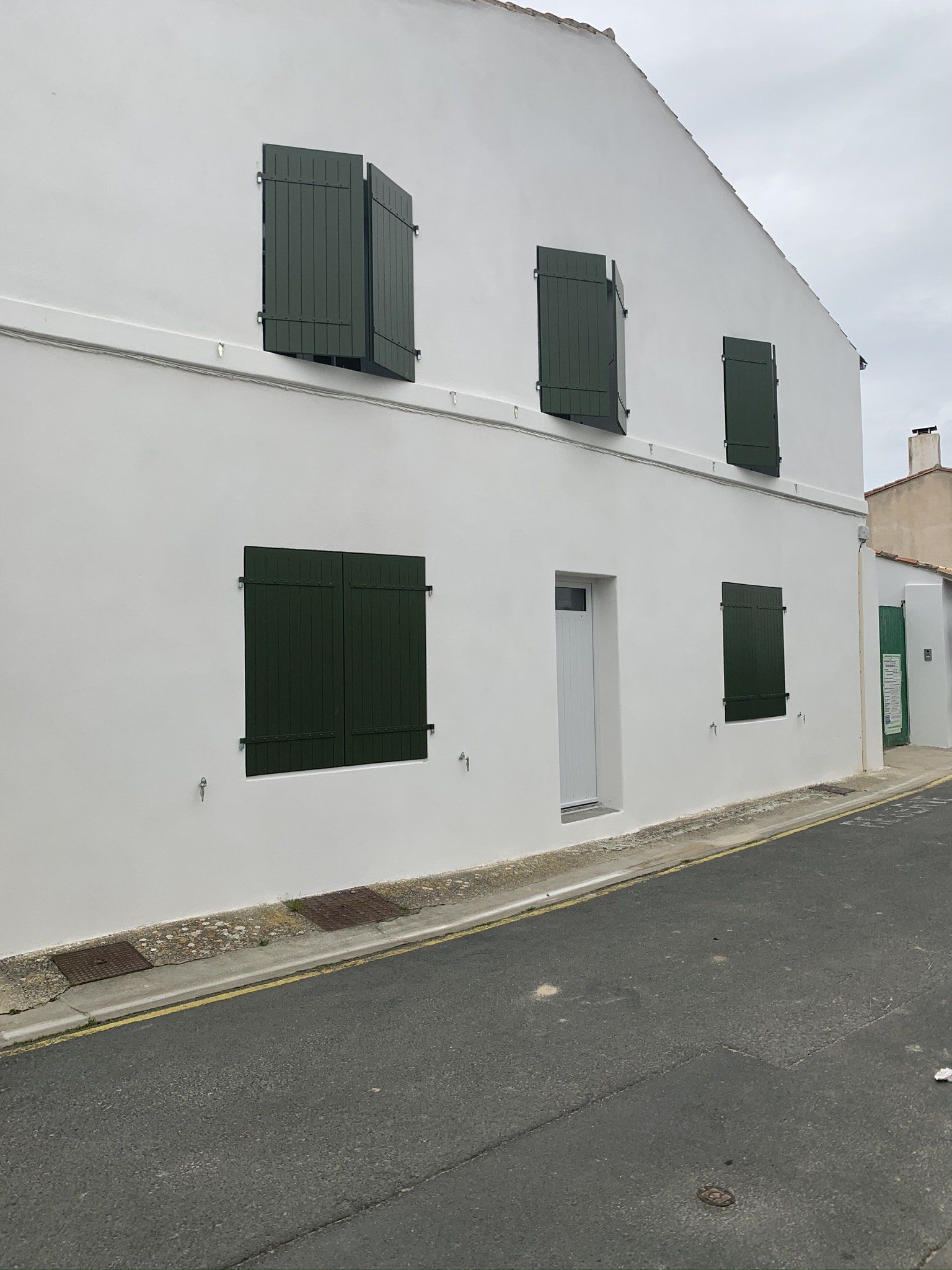 Façade blanche avec une porte et 5 fenêtres fermées par des volets à battants en bois