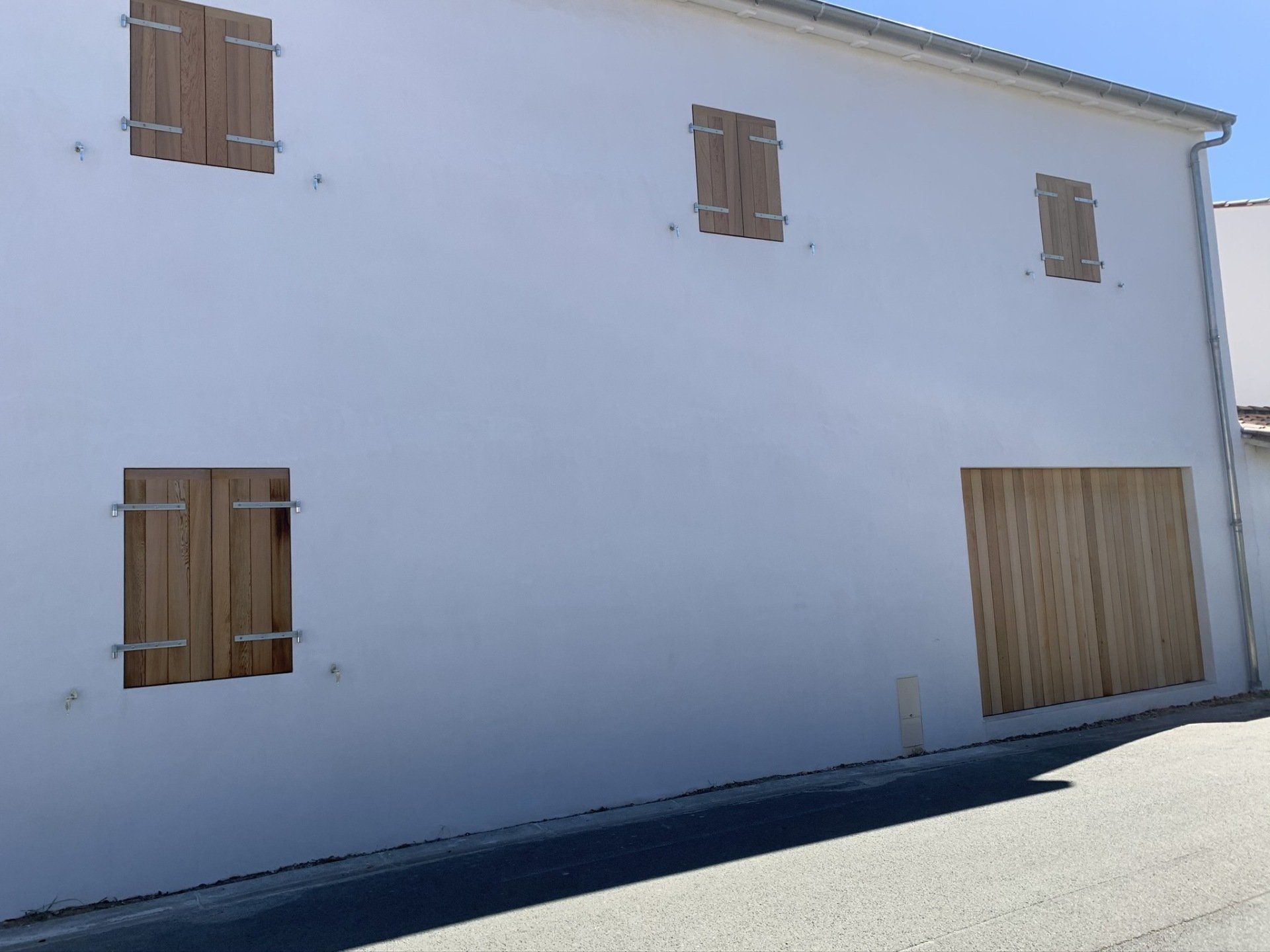 Portail et volets en bois fermés sur une grande façade blanche