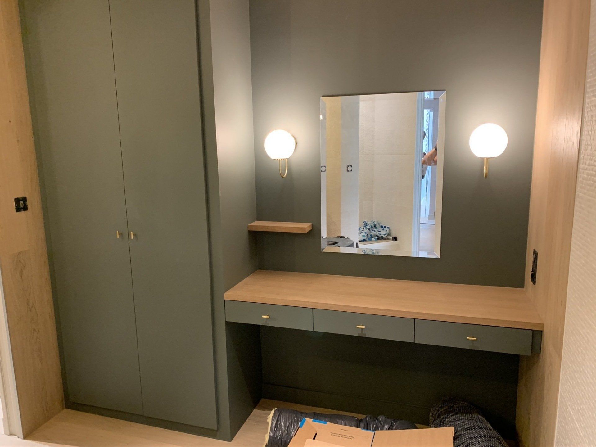 Petit meuble à 3 tiroirs sous un miroir entouré de 2 lampes rondes