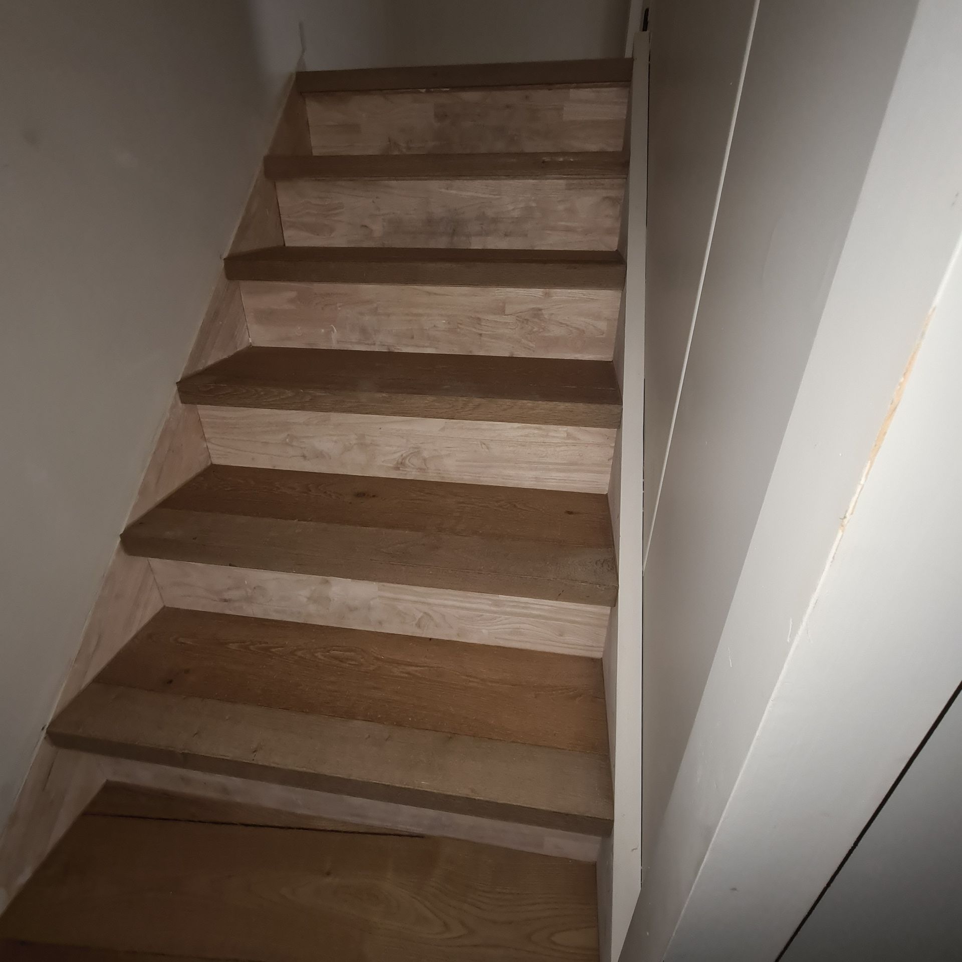 Un escalier étroit aux marches en bois et aux murs blancs.