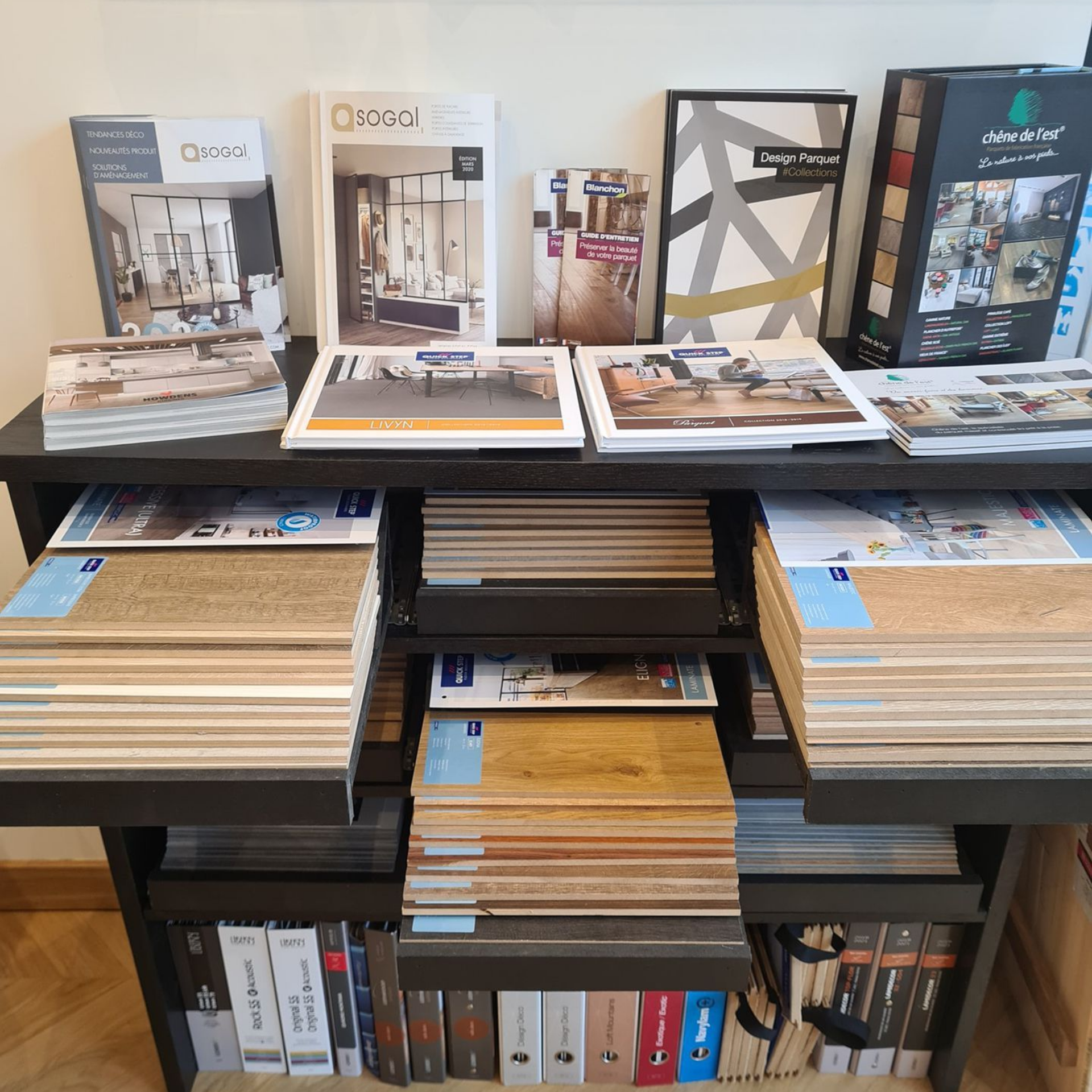 Des catalogues et des échantillons de parquet organisés sur des étagères.