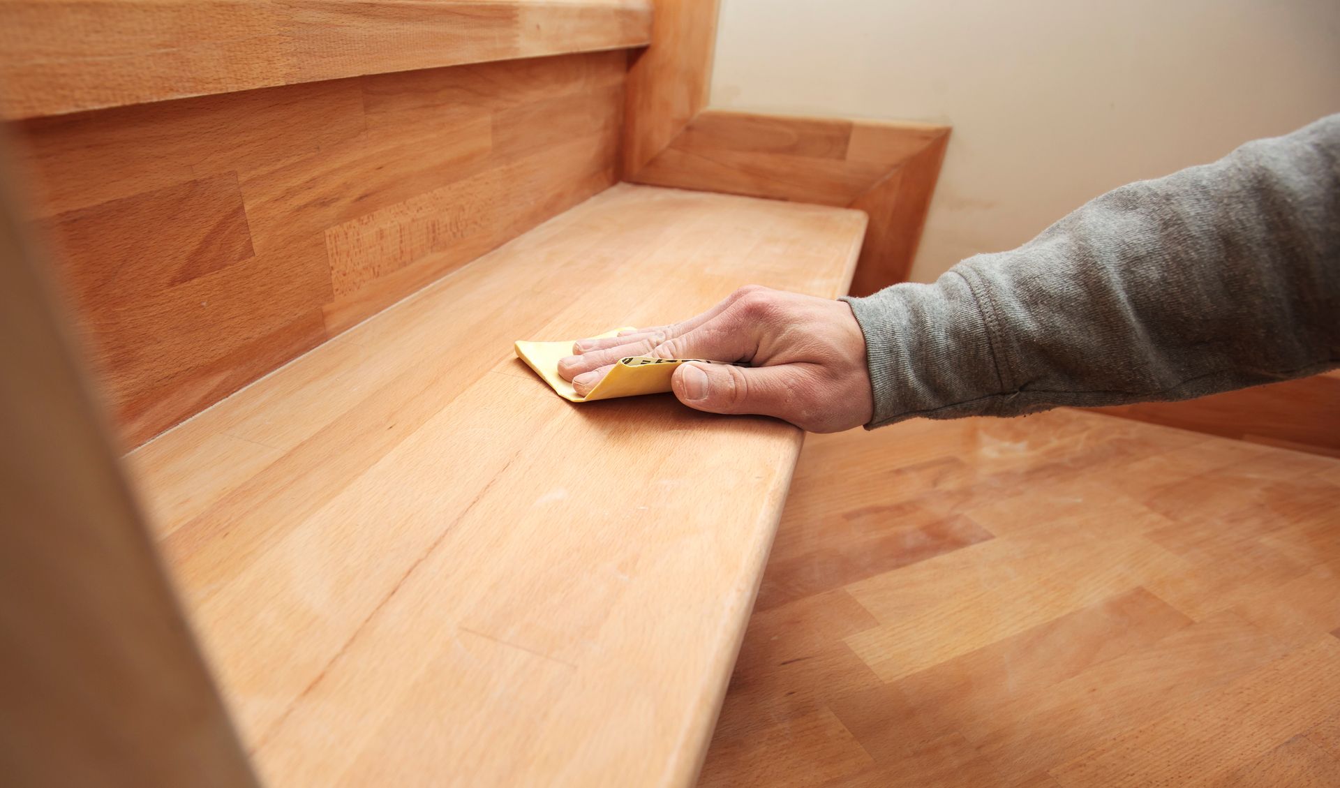 Ponçage manuel d'une marche d'escalier en bois avec un bloc de ponçage.