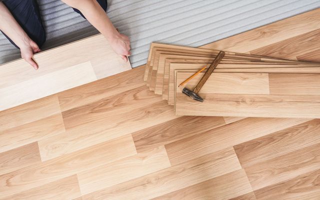 Pose de lames de parquet clair au sol.