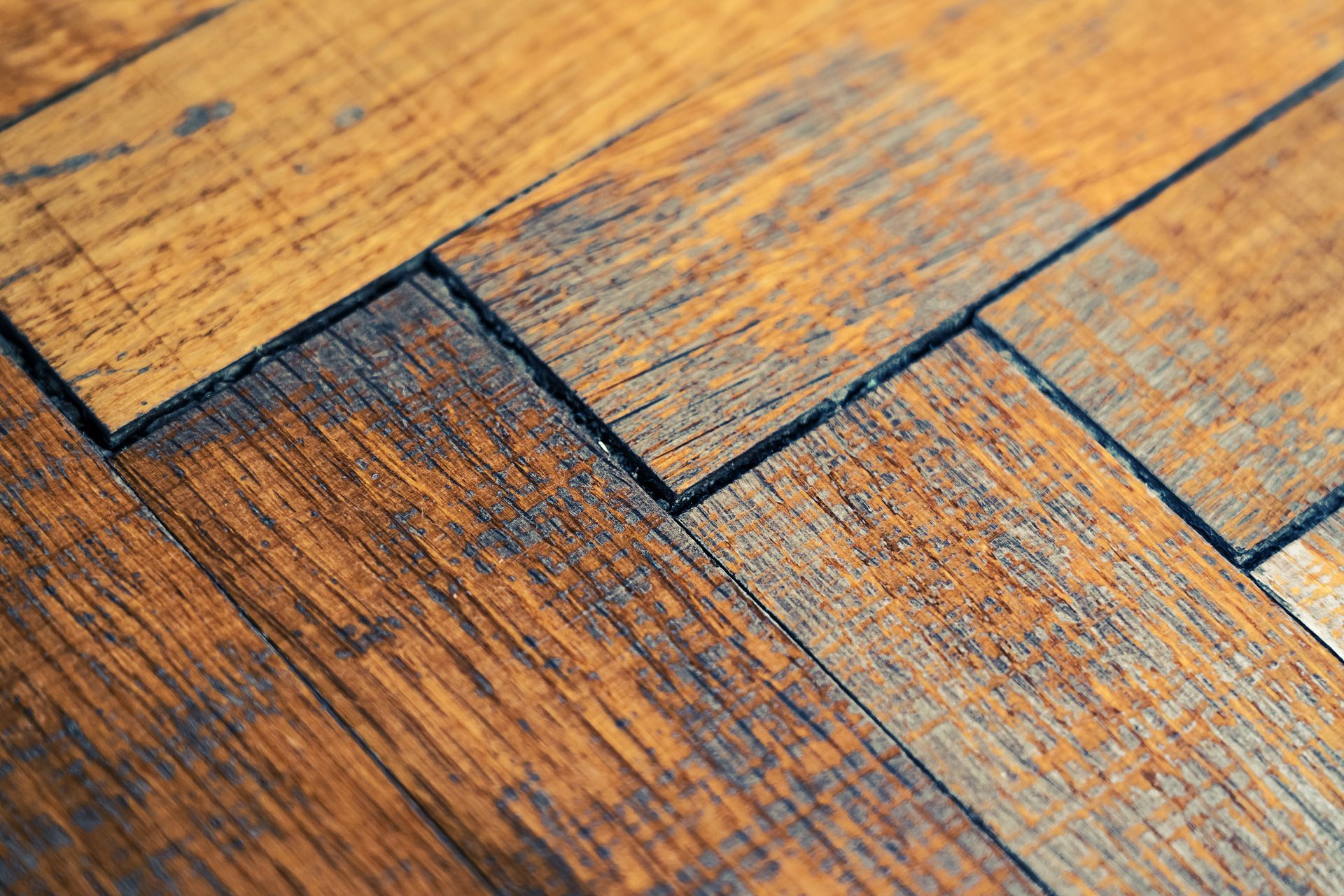 Gros plan sur des planches de parquet patinées, aux joints sombres et au grain brun orangé.