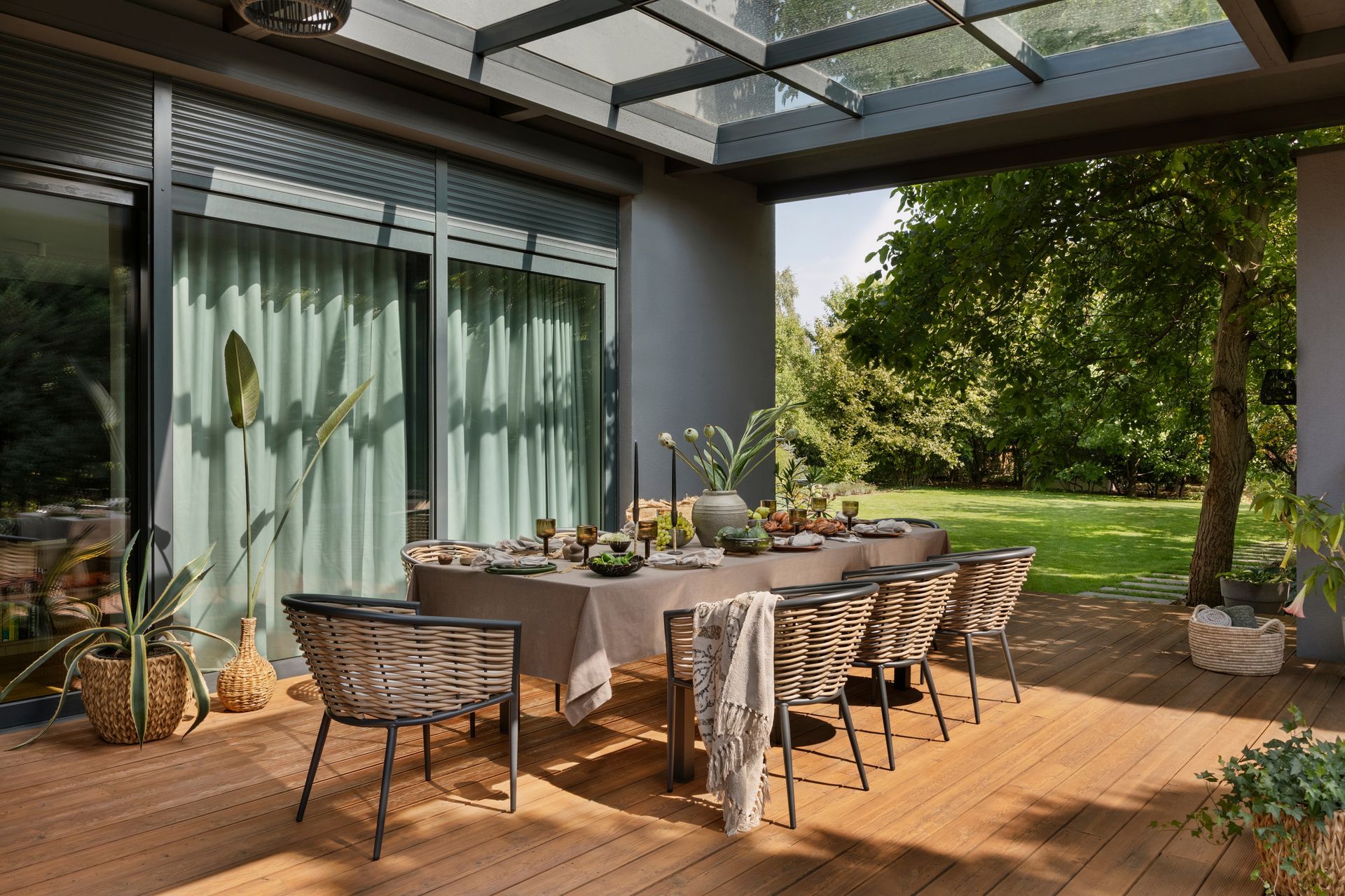 Une grande table à manger sur une terrasse en bois, à l'extérieur d'une maison.