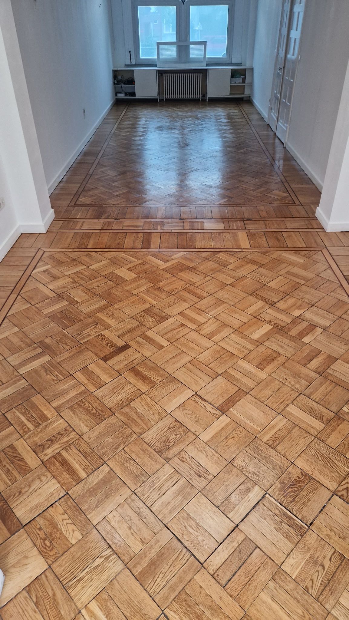 Une pièce vide aux murs blancs, avec un parquet vitrifié au sol.