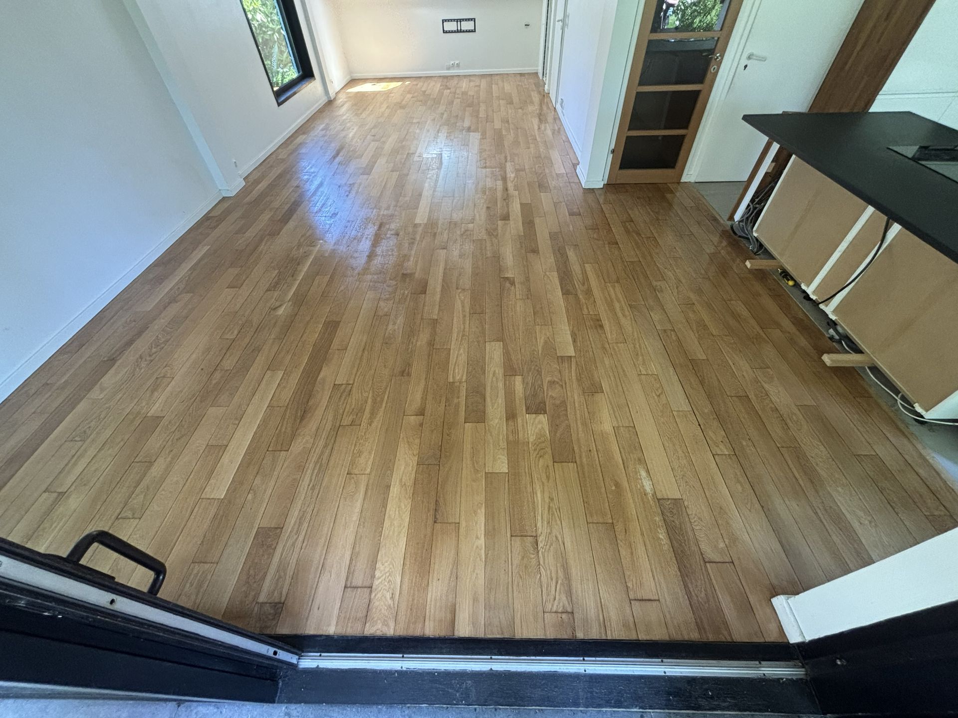 Pièce vide avec un parquet clair, des murs blancs et un comptoir foncé.