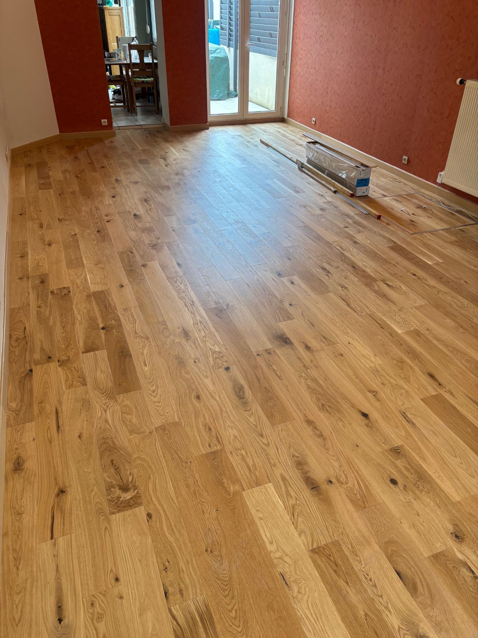 Une pièce vide avec des murs rouges et un parquet au sol.